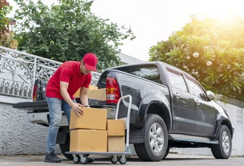 Delivery man in red uniform unloading cardboard boxes from pickup truck