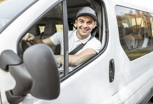 Portrait of a cheerful delivery driver in uniform looking out the window of the white crew van vehicle