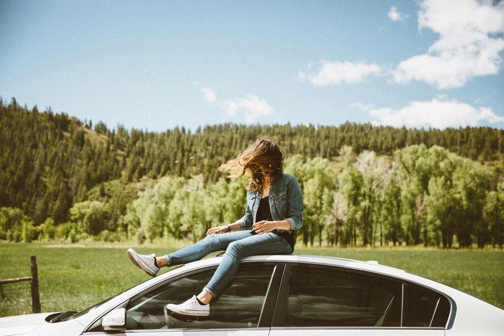 Young woman in denim sitting on car roof