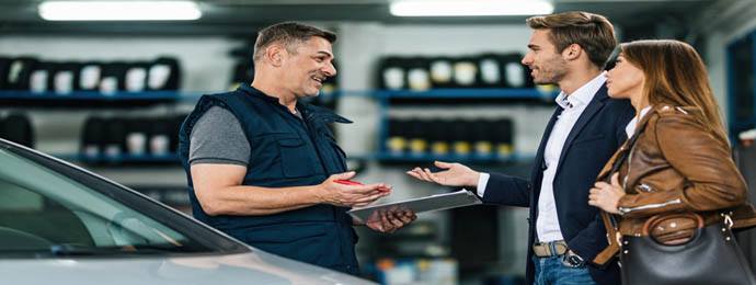 Young happy couple talking to car mechanic in auto repair shop