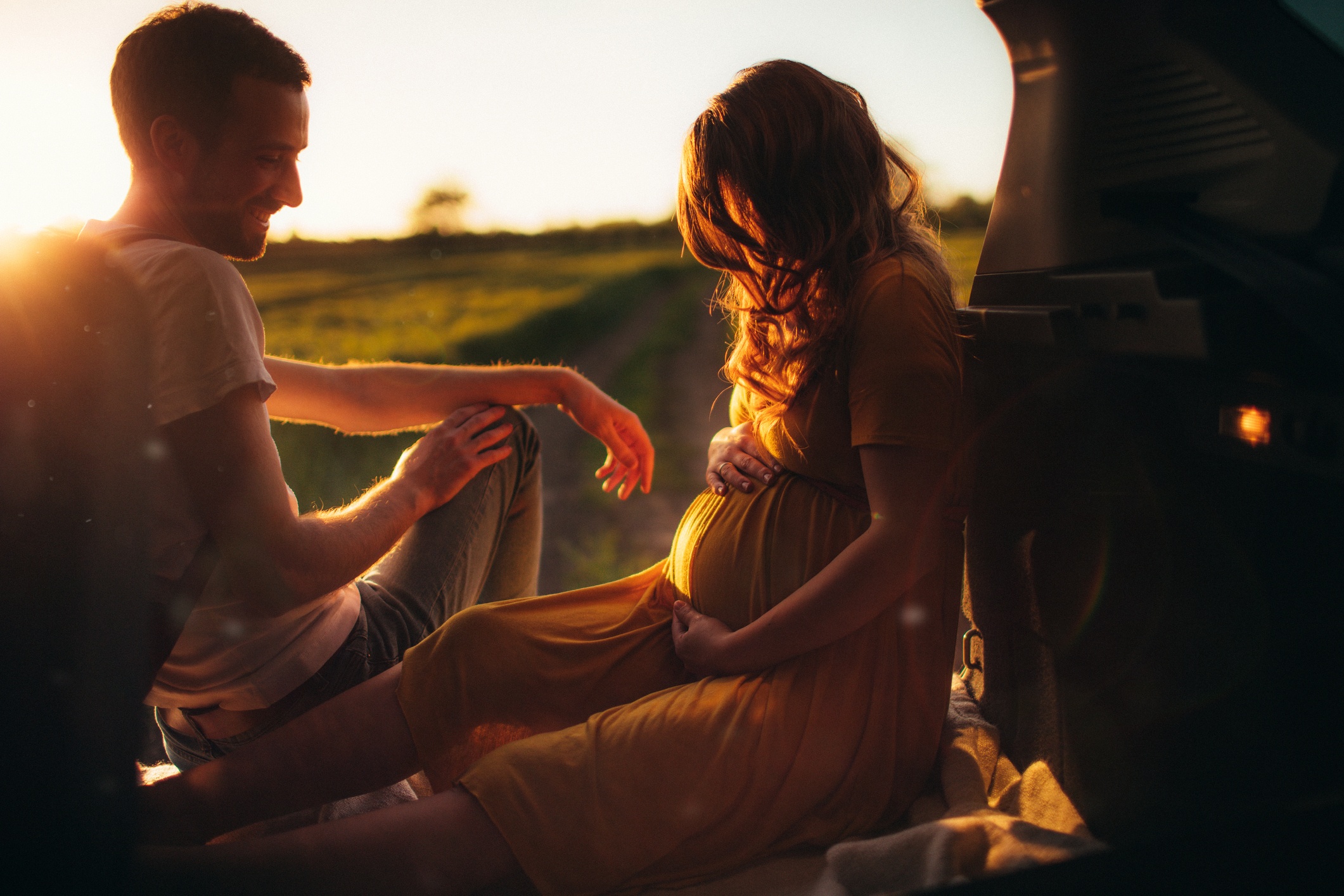 pregnant woman with her partner relaxing outside next to a car