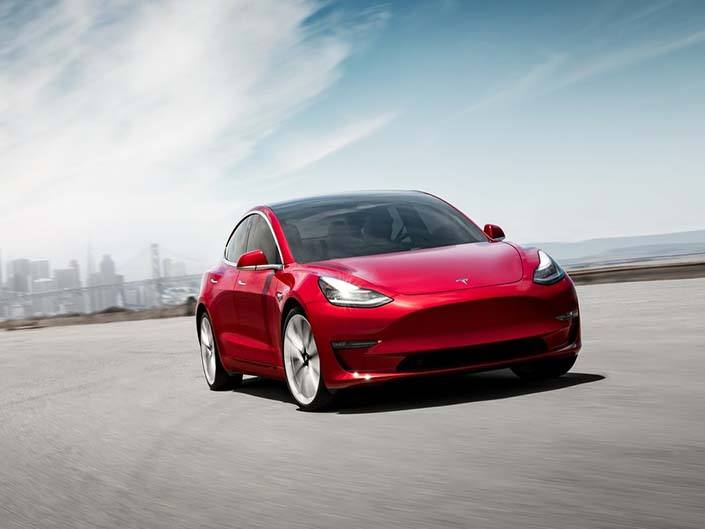 A red Tesla Model 3 driving on an open road