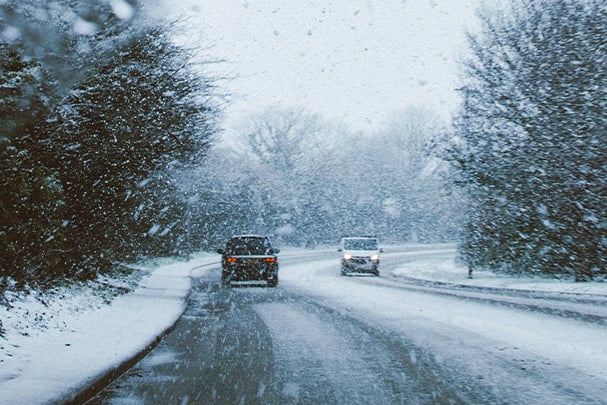 two cars driving on a snowy road intersecting a forest