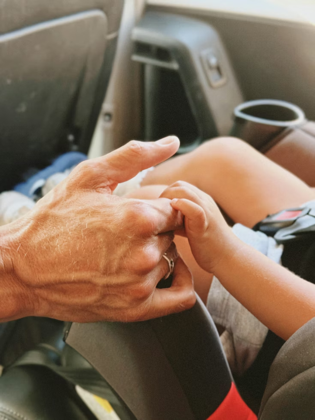 adult hand holding a childs hand in car