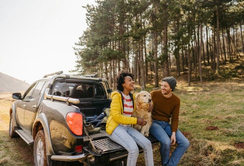 Couple sitting on a pickup truck with a dog