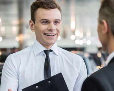 car dealer with clipboard talking to customer