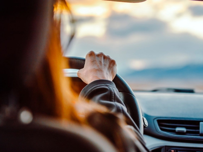 Close-up of a woman's hand on the steering wheel while driving with a scenic view ahead.