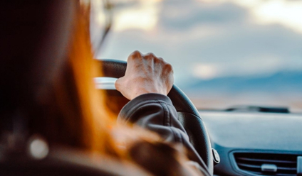 Close-up of a woman's hand on the steering wheel while driving with a scenic view ahead.