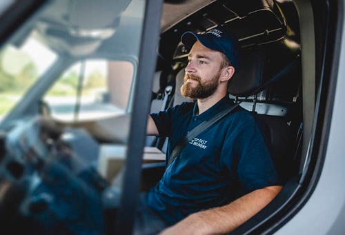 Side view of confident young independent delivery expert sitting in driver’s seat of van ready to begin transport