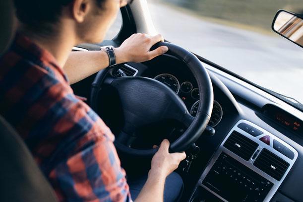 Close up of young man with hands on car steering wheel.