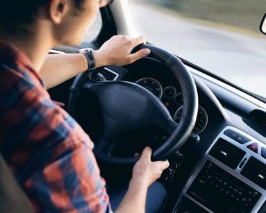 Close up of young man with hands on car steering wheel.