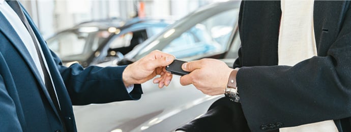 A Person Giving a Car Key To Another Person While Shaking His Hands