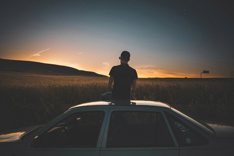 Man sitting on roof of car with sunset in background