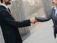 Man and woman in business attire shaking hands outdoors.
