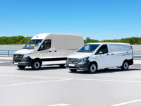 Two white delivery vans parked in a spacious parking lot under a clear blue sky.