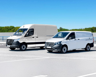 Two white delivery vans parked in a spacious parking lot under a clear blue sky.
