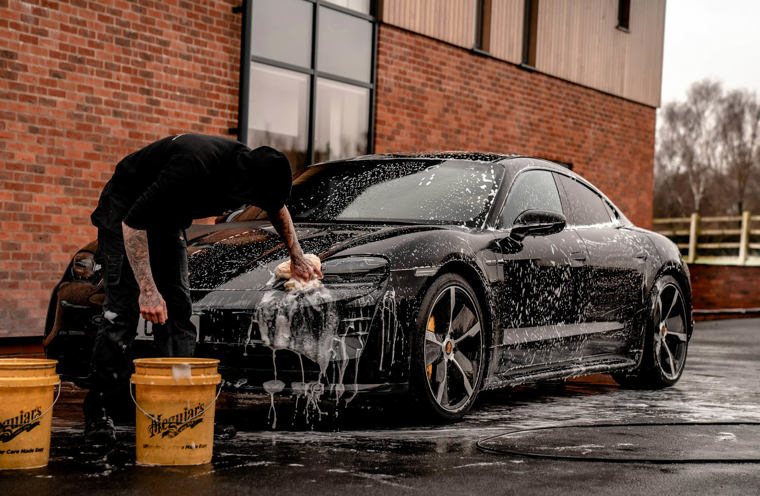 Person washing black sports car with a sponge