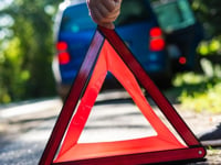Close-up of a hand placing an emergency warning triangle by a car.