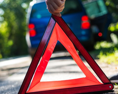 Close-up of a hand placing an emergency warning triangle by a car.
