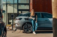 Woman standing next to an EV plugged into charge