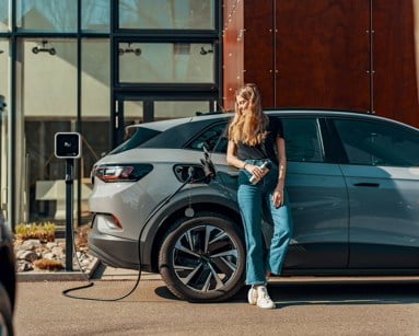 Woman standing next to an EV plugged into charge