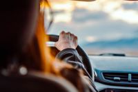 Close-up of a woman's hand on the steering wheel while driving with a scenic view ahead.