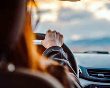 Close-up of a woman's hand on the steering wheel while driving with a scenic view ahead.