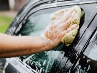 Close up of a person cleaning a black car with a sponge