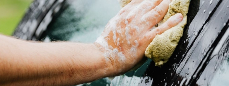 Close up of a person cleaning a black car with a sponge