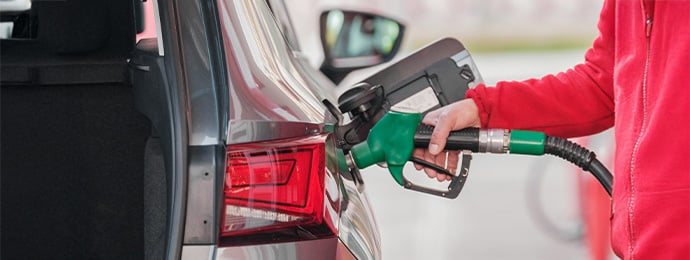 Close-up of a person refuelling a silver estate car with a green petrol pump at a UK fuel station