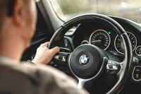 Man driving a bmw with one hand on the steering wheel