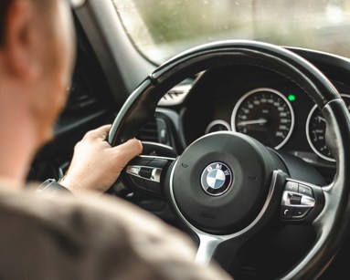 Man driving a bmw with one hand on the steering wheel