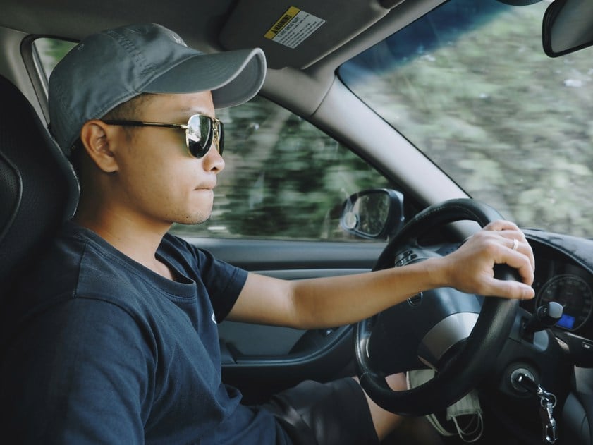 man wearing a hat and sunglasses driving a car