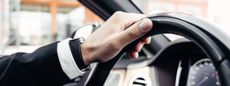 Elegant hand in a suit holding a modern car steering wheel, close-up shot inside a vehicle.