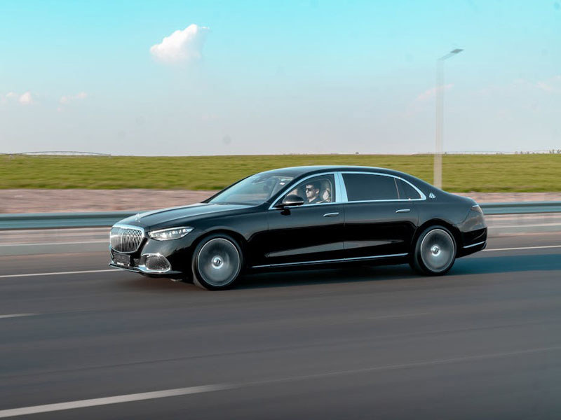 Side on view of a black saloon car driving on the motorway with green fields and a blue sky in the background