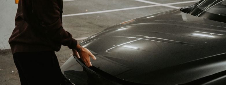 A person opens the car hood in a dimly lit parking garage, showcasing urban transportation.