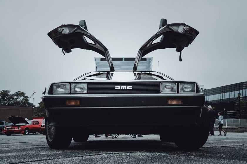 Front view of a vintage DeLorean car with its distinctive gullwing doors open, displayed outdoors.