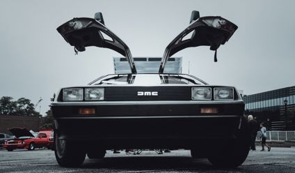 Front view of a vintage DeLorean car with its distinctive gullwing doors open, displayed outdoors.