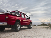 A red pickup truck parked by the rocky coastline under a cloudy sky in Mgarr, Malta.