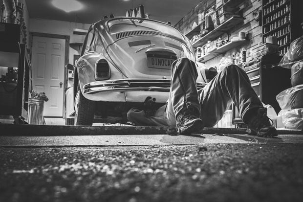 A Black and white photo of a person under a car fixing it