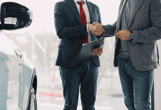 Two men shaking hands in a car dealership, symbolizing a successful business deal.
