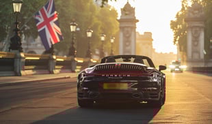 Rear view of a black Porsche 911 Cabriolet driving on a London street at sunrise