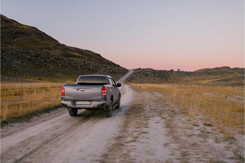Grey pickup truck driving on a dirt track with mountain in background