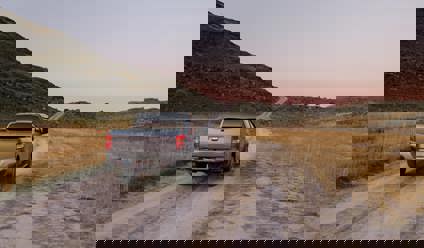 Grey pickup truck driving on a dirt track with mountain in background