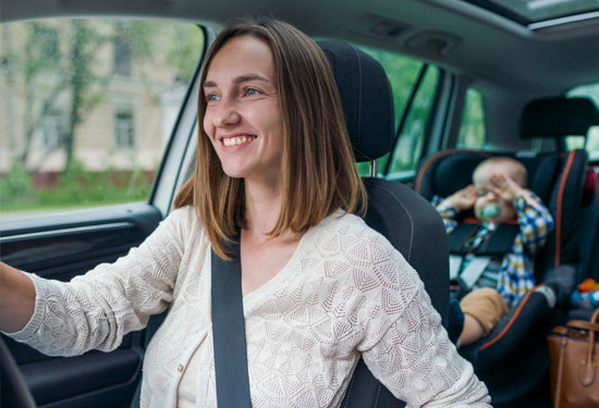 Beautiful smiling woman driving a car with little baby on the backseat