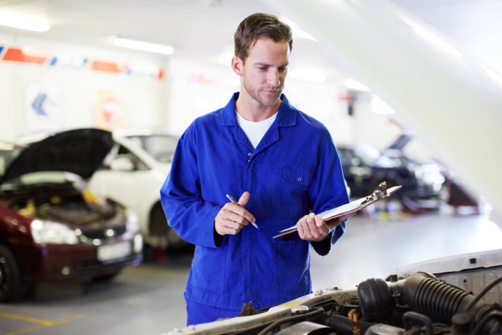 A mechanic holding a clipboard and performing checks on a vans engine