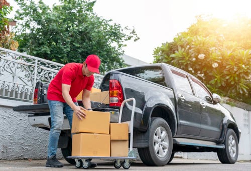 Delivery man in red uniform unloading cardboard boxes from pickup truck