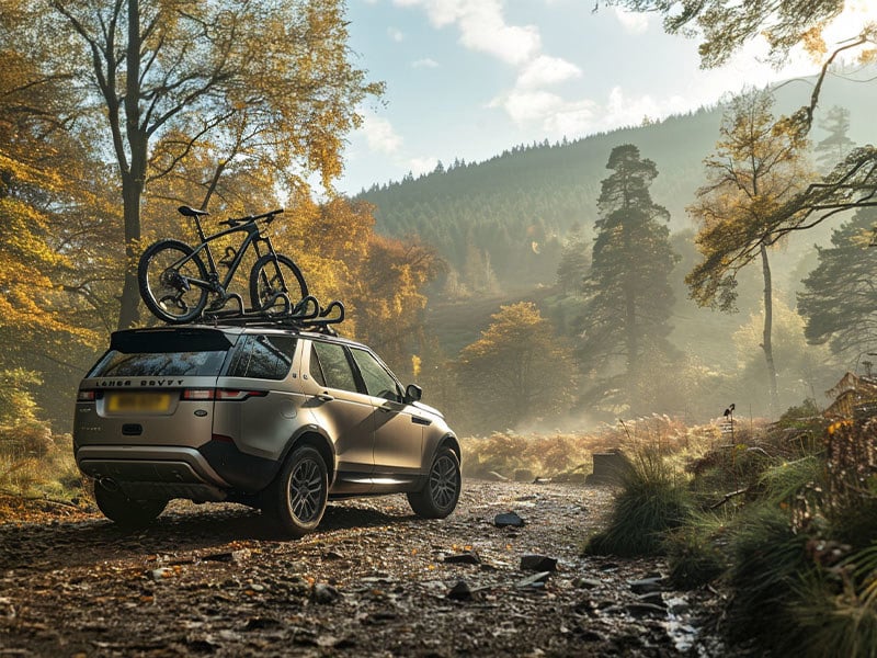 Land Rover Discovery SUV with a mountain bike on the roof parked on a forest trail in autumn