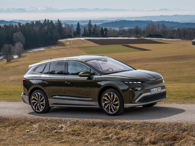 Front-side on view of a Skoda Enyaq SUV driving on a country road with a forest in the background