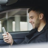 man smiling while looking at his phone in car